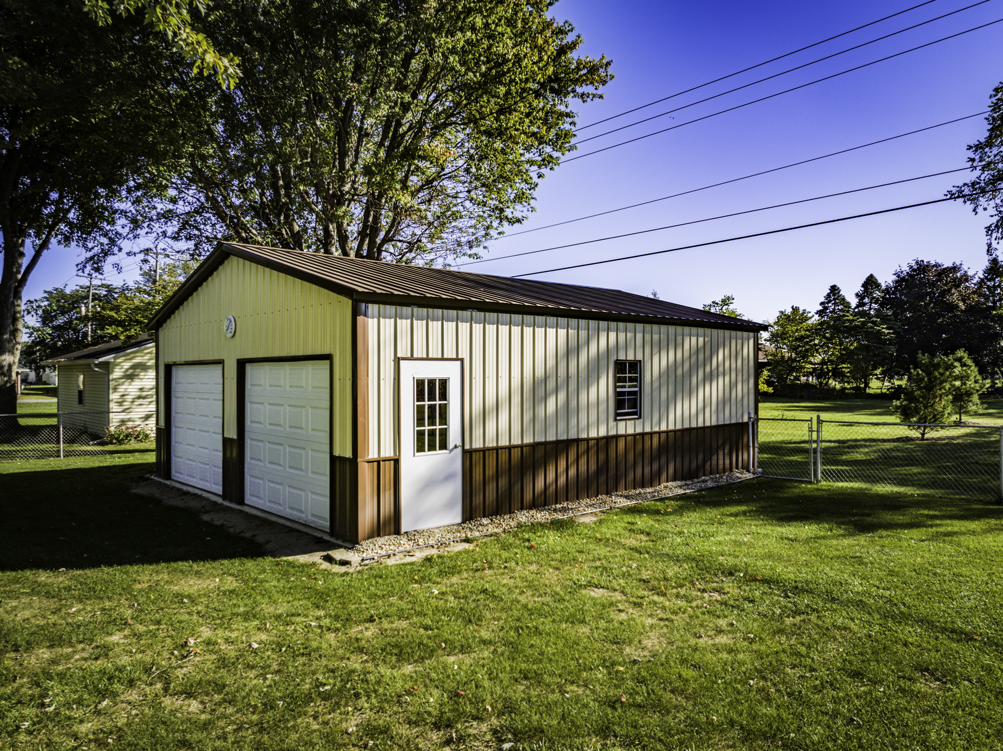 A tan and brown metal garage surrounded by trees and grass.